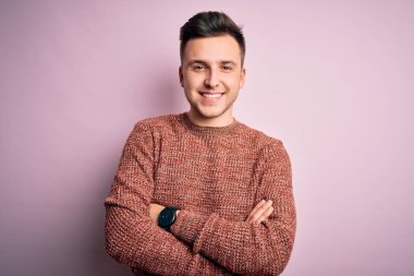 Pembe izole edilmiş arka planda sıradan bir kazak giyen, kollarını kavuşturup kameraya gülümseyen yakışıklı beyaz bir adam. Pozitif kişi.