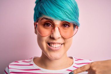 Mavi saçlı, kuku gözlüklü, kalbi olan, kendini işaret eden genç ve güzel bir kadın.