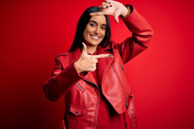 Genç, güzel, esmer, günlük ceket giyen, kırmızı arka planda duran, gülümseyen, elleri ve parmakları mutlu yüzlü bir kadın. Yaratıcılık ve fotoğrafçılık kavramı.