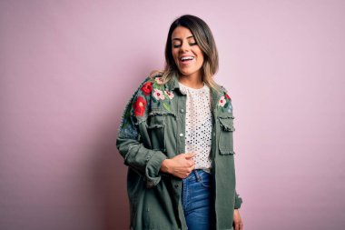 Moda kıyafetleri giyen genç ve güzel bir kadın. Manken, sokak tarzı giyiniyor. Pembe arka planda dikiliyor.