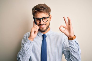 Genç işadamı beyaz arka planda akıllı telefondan konuşuyor. Tamam işareti yapıyor. Mükemmel bir sembol.