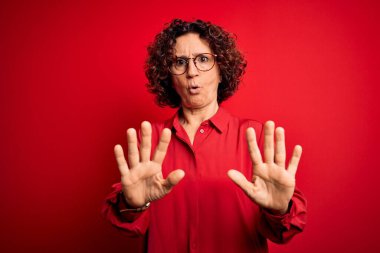 Orta yaşlı, kıvırcık saçlı, günlük gömlek ve gözlük takan güzel bir kadın kırmızı arka planda el ele tutuşup reddediyor ve iğrenç bir ifadeyle reddediyor. Dur ve yasakla.