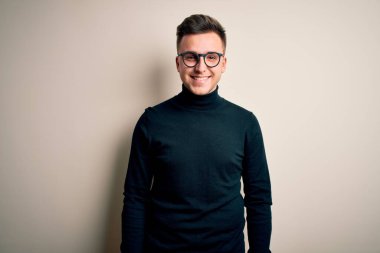 Gözlük takan yakışıklı beyaz bir adam ve izole edilmiş arka planda rahat bir süveter, yüzünde mutlu ve havalı bir gülümsemeyle. Şanslı kişi..