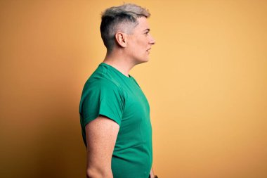Sarı arka plan üzerine gündelik yeşil tişört giyen genç, yakışıklı ve modern bir adam rahat bir görünüm ve kendine güvenen bir gülümseme takınıyor..