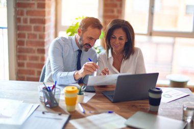 Mutlu ve kendinden emin gülümseyen iki orta yaşlı iş adamı. Ofiste dizüstü bilgisayarla gülümseyerek birlikte çalışıyoruz.