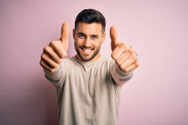 İzole edilmiş pembe arka plan üzerinde duran genç ve yakışıklı bir adam el hareketini onaylıyor, gülümsüyor ve başarı için mutlu. Kazanan jest.