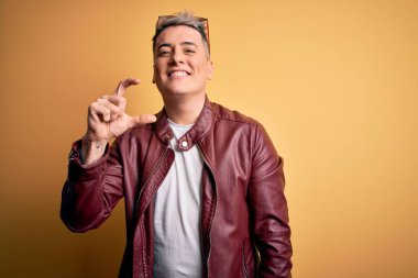 Genç, yakışıklı, deri ceket ve sarı arka planda güneş gözlüğü takan, gülümseyen, kendine güvenen, el hareketi yapan, parmaklarıyla işaret yapan ve kameraya bakan modern bir adam. Ölçü kavramı.