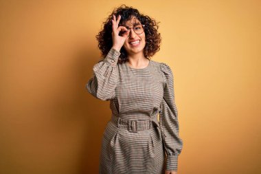 Güzel bir Arap iş kadını. Elbise ve gözlük takıyor. Sarı arka planda duruyor..