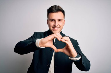 Zarif bir kışlık ceket giyen genç yakışıklı iş adamları izole edilmiş arka planda durup aşka gülümsüyor ve elleriyle kalp sembolü yapıyor. Romantik konsept.