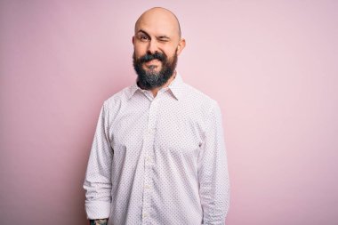 Yakışıklı, kel, sakallı, zarif tişörtlü, soyutlanmış pembe arka planda, kameraya seksi bir ifadeyle bakıyor, neşeli ve mutlu bir yüzle..