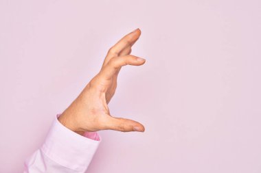 İzole edilmiş pembe arka plan üzerinde parmaklarını gösteren beyaz bir adamın eli. Görünmez bir şeyi alıp, parmaklarıyla uzayı gösteren bir nesneyi tutuyor.