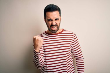 Sakallı, normal çizgili t-shirt giyen genç ve yakışıklı bir adam beyaz arka planda kızgın ve kızgın duruyor öfkeyle bağırırken yumruğunu kaldırıyor. Öfke ve agresif kavram.