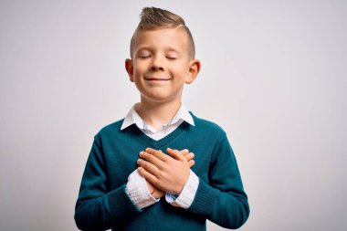 Mavi gözlü küçük beyaz çocuk soyutlanmış arka planda zarif giysiler giyip ellerini göğsüne koyup gülümsüyor ve yüzünde minnet dolu bir jest var. Sağlık kavramı.