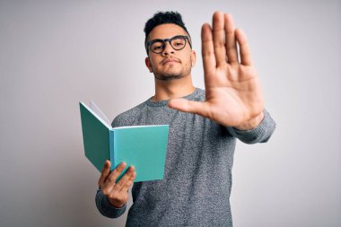 Yakışıklı, zeki bir öğrenci, izole edilmiş beyaz arka plan üzerinde kitap okuyor. El açık, dur işareti yapıyor. Ciddi ve kendinden emin bir ifadeyle, savunma jesti.