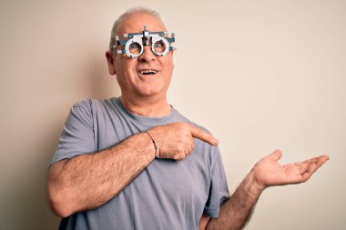 Beyaz arka planda optometri gözlüğü takan orta yaşlı, ağarmış adam kameraya hayret ediyor ve gülümsüyor..