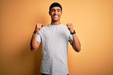 Sarı arka plan üzerine spor giyerek spor yapan yakışıklı Afro-Amerikan sporcusu. Kolları havada ve gözleri kapalı zaferi gülümseyerek kutluyor. Kazanan konsept.