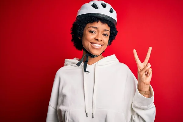 若いアフリカ系アメリカ人のアフリカ人自転車のセキュリティヘルメットを着て巻き毛の女性が勝利の兆候を行うカメラでの幸せな顔のウィンクで笑みを浮かべてサイクリング 第二番 — ストック写真