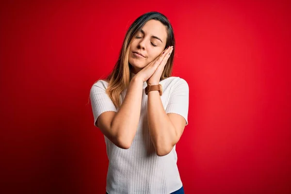 美しいですブロンド女性で青い目を身に着けていますカジュアル白いTシャツ上の赤い背景睡眠疲れ夢を見て 一緒に手でポーズしながら笑顔で閉じた目 — ストック写真