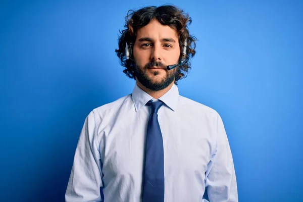 青い背景にヘッドセットを使用して顔に真剣な表情で作業髭を生やした若いハンサムなコールセンターエージェントの男 シンプルで自然なカメラを見て — ストック写真
