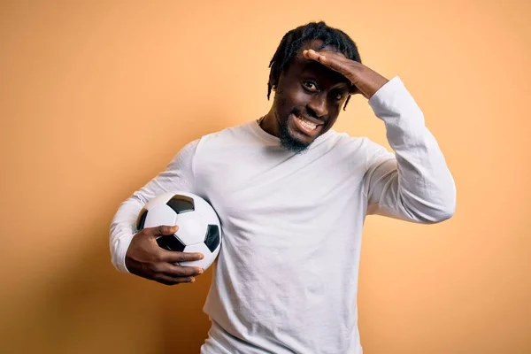 Young african american player man playing soccer holding football ball over yellow background stressed with hand on head, shocked with shame and surprise face, angry and frustrated. Fear and upset for mistake.
