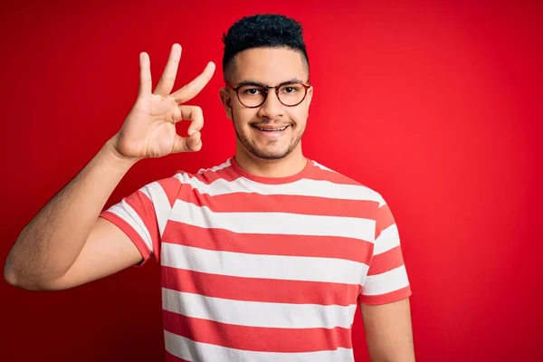 Mladý Pohledný Muž Neformálním Pruhovaném Tričku Brýlích Izolovaném Červeném Pozadí — Stock fotografie