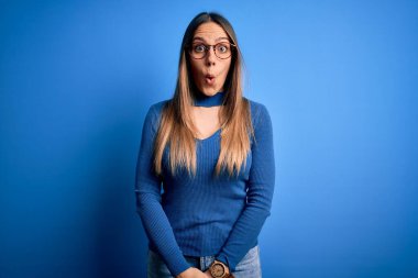 Mavi gözlüklü, genç, sarışın bir kadın mavi arka planda korku, korku ve heyecan dolu bir yüz ifadesiyle dehşete düşmüş ve şok olmuştu..