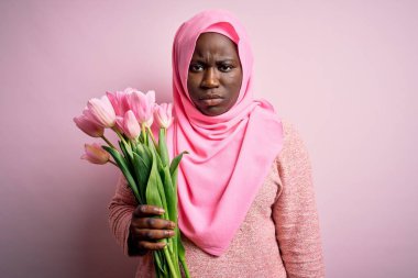Genç Afro-Amerikan artı cüsseli kadın elinde pembe lale buketi tutan kuşkucu ve gergin sorunlar yüzünden surat asıyor. Negatif kişi.