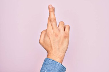 İzole edilmiş pembe arka plan üzerinde parmaklarını gösteren beyaz bir gencin eli. Parmakları çapraz, batıl inançlar ve şanslı bir jest, şanslı ve umut dolu bir ifade.