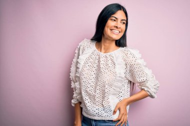 Moda kıyafetleri giyen genç ve güzel bir kadın. Manken, sokak tarzı giyiniyor. Pembe arka planda dikiliyor.