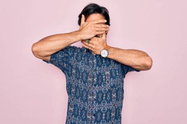 Pembe arka planda hippi tarzı giyinen yakışıklı İspanyol bohem adam gözleri ve ağzı kapalı, şaşırmış ve şok olmuş. Duygularını gizliyor.