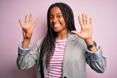 Genç Afrikalı Amerikalı iş kadını pembe izole edilmiş arka planda duruyor ve dokuz numaralı parmaklarıyla işaret ederken kendinden emin ve mutlu gülümsüyor..