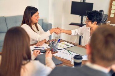 Bir grup iş adamı mutlu ve kendinden emin gülümsüyor. Birlikte çalışırken gülümseyerek ofiste el sıkışırken.