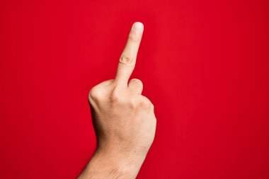 Hand of caucasian young man showing fingers over isolated red background showing provocative and rude gesture doing fuck you symbol with middle finger