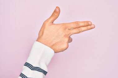 İzole edilmiş pembe arka planda parmaklarını gösteren beyaz bir gencin eli. Ateşli tabancayı parmaklarıyla işaret ediyor.