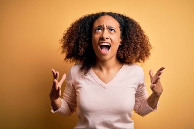 Afro saçlı, sarı arka planda rahat süveter giyen, deli gibi bağıran, agresif ifade ve kollarıyla bağıran Afro-Amerikalı genç bir kadın. Hayal kırıklığı konsepti.