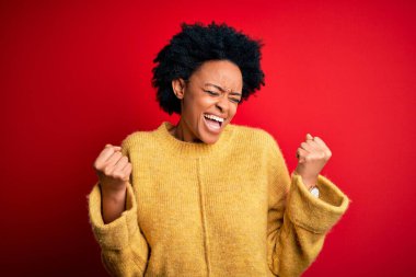 Kıvırcık saçlı, mutlu ve heyecanlı bir şekilde kolları havada, gülümseyen ve başarı için bağıran genç Afro-Amerikan kadın. Kutlama konsepti.