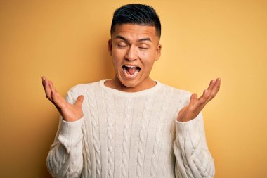 Sarı arka plan üzerine beyaz süveter giyen genç, yakışıklı, Latin bir adam kollarını kaldırıp heyecanla haykırarak başarının çılgınlığını kutluyor. Kazanan konsept