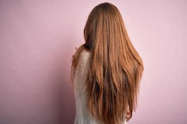 Genç, güzel, kızıl saçlı bir kadın pembe arka planda günlük süveter ve gözlük takıyor. Kendine mutlu ve pozitif bir şekilde sarılıyor. Sevgi ve özgüven.