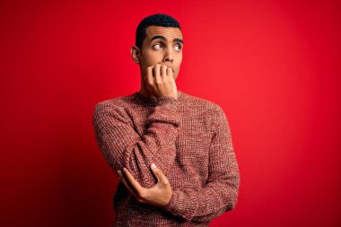 Genç ve yakışıklı Afro-Amerikan bir adam kırmızı arka planda dikilmiş elleri ağız ısıran, gergin ve sıradan bir süveter giyiyor. Endişe sorunu.
