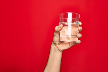Güzel bir el, bir bardak suyu izole edilmiş kırmızı arka planda tutuyor.