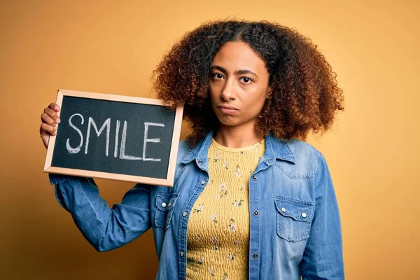 Young african american woman with afro hair holding blackboard with smile message with a confident expression on smart face thinking serious