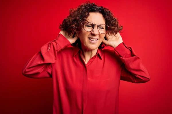 中年美丽的卷发女人 身穿宽松的衬衫 戴着一副红色背景的眼镜试图听到两只手在耳朵上的手势 好奇地闲聊 听力问题 — 图库照片