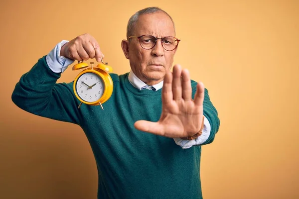 Senior Stilig Man Som Håller Väckarklocka Stående Över Isolerad Gul — Stockfoto