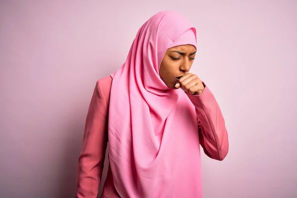 若いアフリカ系アメリカ人アフリカ人女性は 孤立したピンクの背景にイスラム教徒のヒジャーブを身に着けており 風邪や気管支炎の症状として咳をしています ヘルスケアの概念 — ストック写真