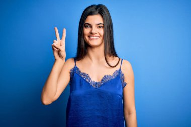 Zarif ve rahat mavi iç çamaşırı giyen genç, güzel esmer kadın iki numarayı gösterip gösterirken kendinden emin ve mutlu bir şekilde gülümsüyor..