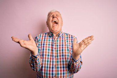 Üst düzey yakışıklı beyaz adam, pembe arka plan üzerine gündelik bir tişört giyip kollarını kaldırmış ve gözleri kapalı heyecanla haykırarak başarının çılgınlığını kutluyor. Kazanan konsept