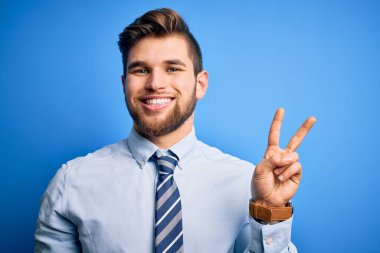 Sakallı, mavi gözlü, şık gömlekli ve kravatlı genç sarışın işadamı iki numaralı parmaklarıyla ayakta duruyor ve gülümsüyor, kendinden emin ve mutlu..