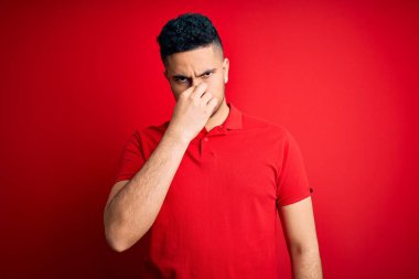 İzole edilmiş arka planda kırmızı polo giyen genç yakışıklı bir adam pis ve iğrenç bir koku alıyor. Dayanılmaz bir koku. Parmakları burnunda nefesini tutuyor. Kötü kokuyor.