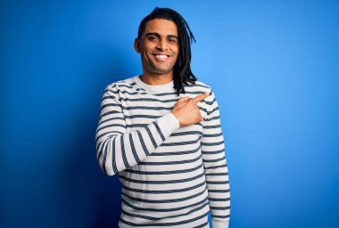 Rastgele çizgili süveter giyen, yüzünde gülücükler açan, mutlu ve doğal bir ifadeyle elini ve parmağını kaldıran Afro-Amerikan genç adam.
