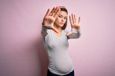 Genç, güzel bir kız hamile, pembe arka planda bebek bekliyor. El ve parmakları kullanarak çerçeveler yapıyor. Kamera bakış açısıyla.